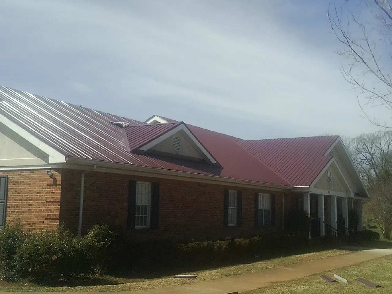 Red metal roof with gabled entries on a long brick building, from a Hail Damage Roof Repair job in Theresa