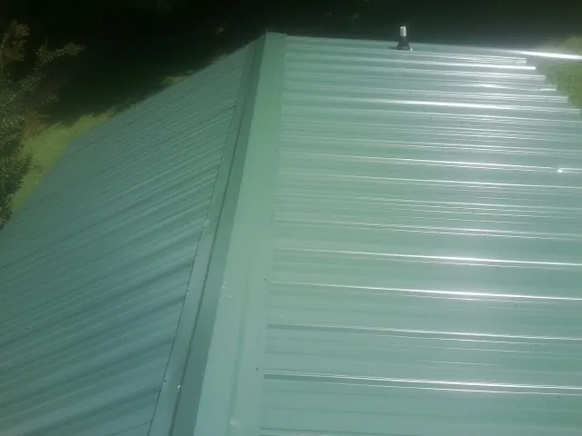 New green metal panels meeting at the ridge of a roof — Flat Roof Repair work by our crew in Theresa
