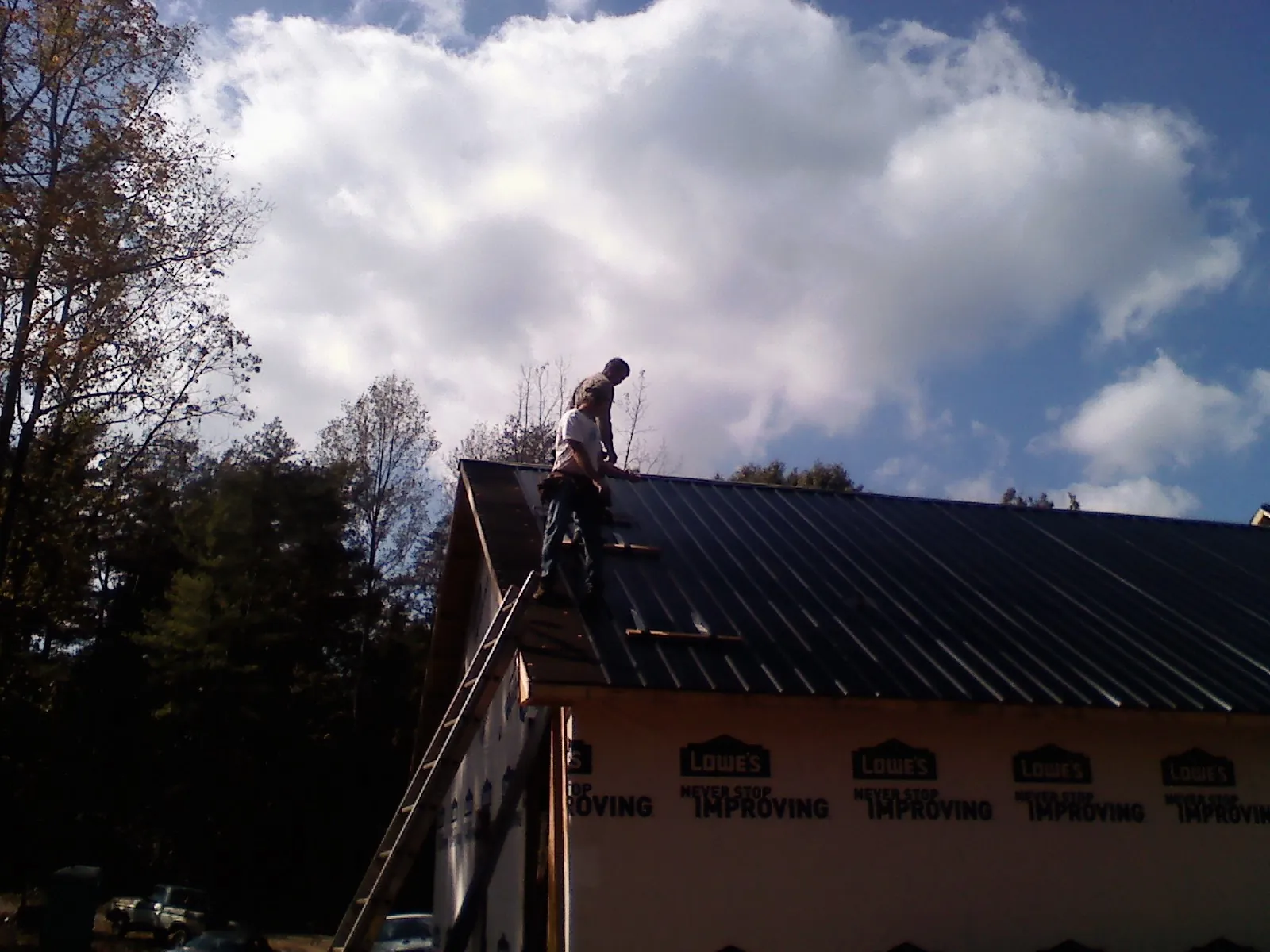 Roofer fastening dark metal panels high against a cloudy sky, from a Roof Inspection job in Theresa