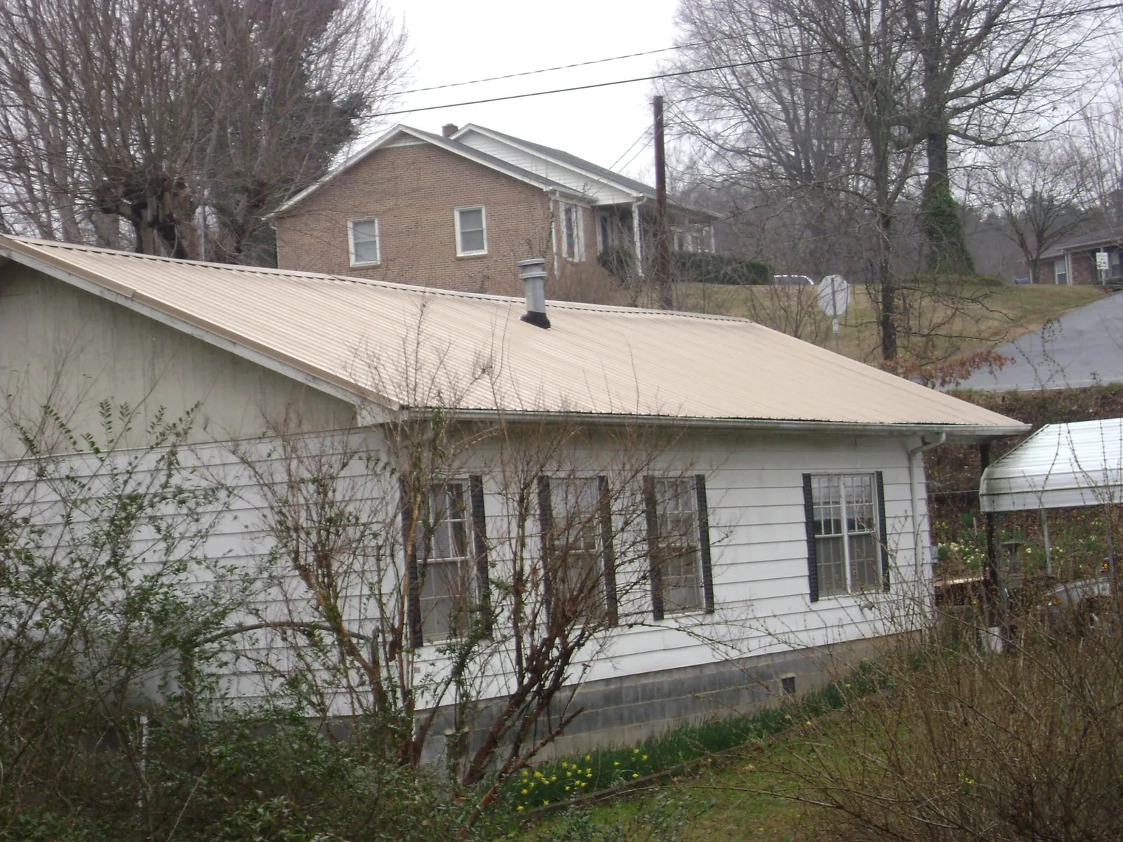 Tan metal roof on a white sided house set into a hillside — Commercial Roofing by Roofing Brothers in Theresa