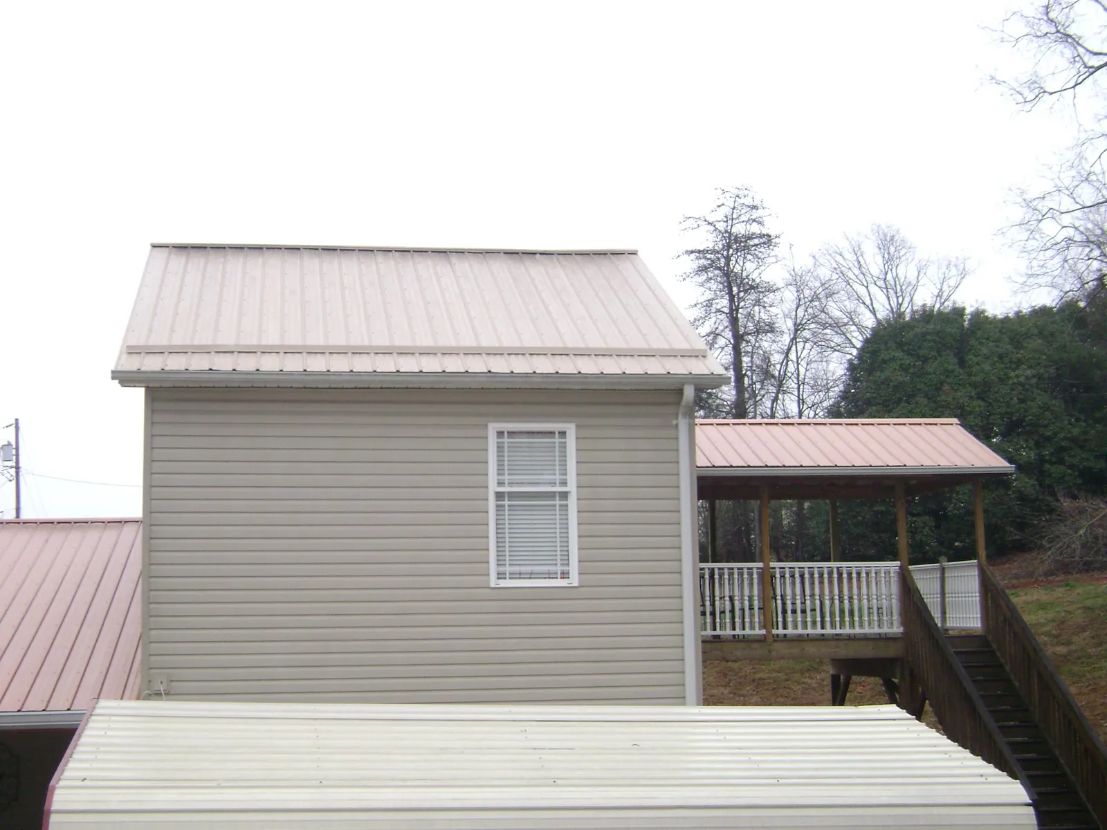 Tan metal roofs on a two story addition and attached porch, from a Roof Replacement job in Theresa