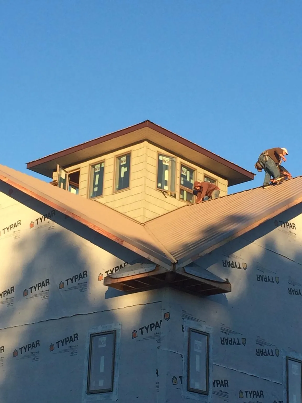 Roofers working around a rooftop cupola on a new metal roof at sunset — Roof Waterproofing in Theresa by Roofing Brothers
